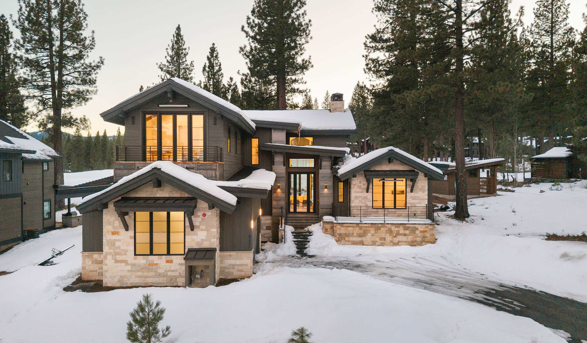 Modern two-story house with a mix of wood and stone facades, large windows, and landscaped garden during daytime.